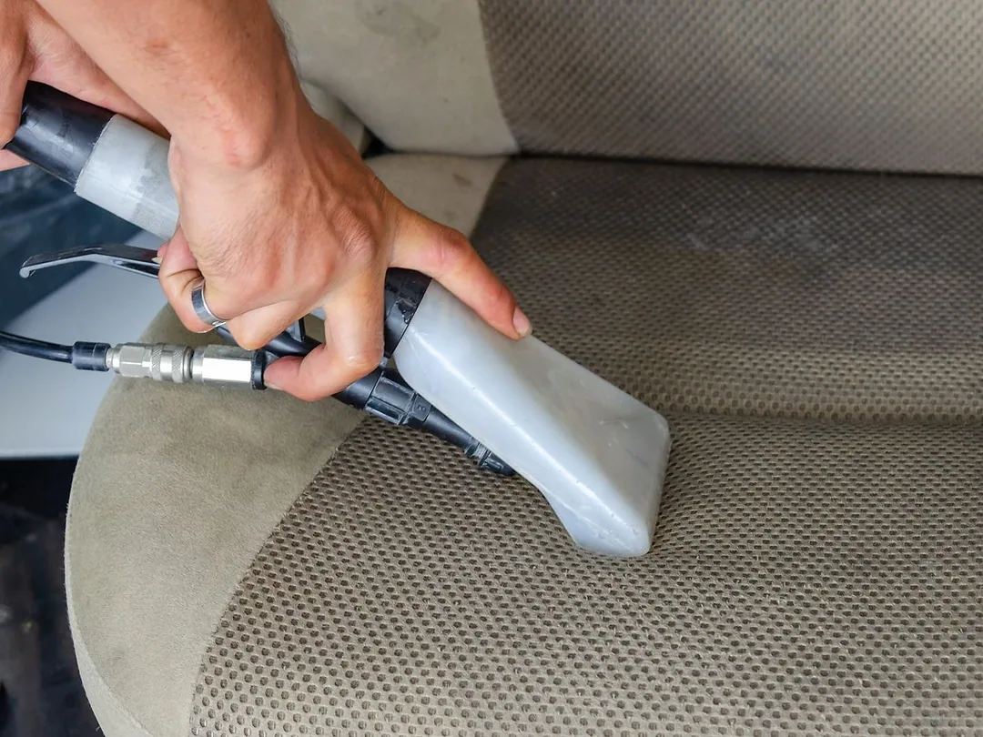 A handheld vacuum cleaning a fabric car seat